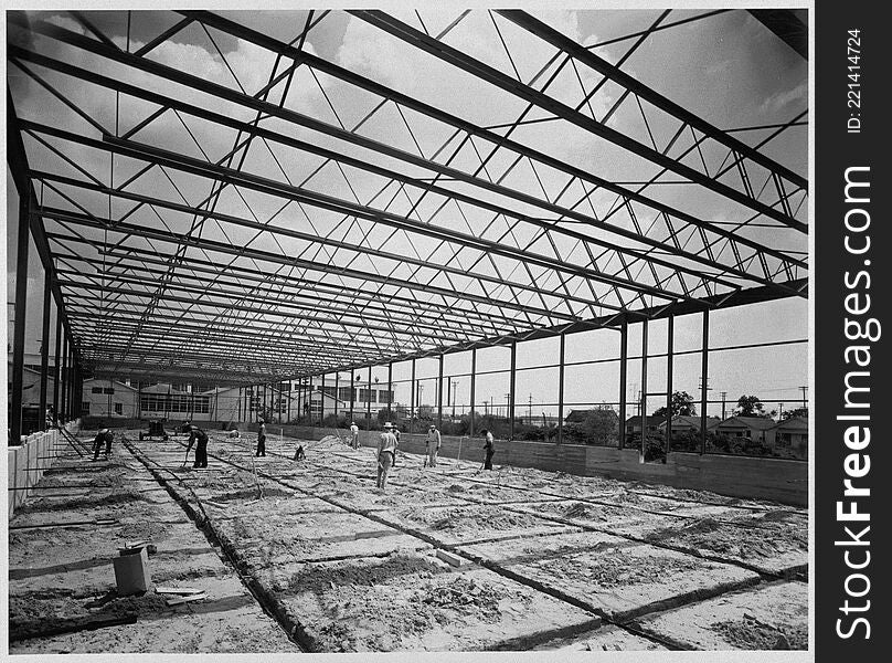 Photograph of a warehouse and office building during construction. The building was constructed by Alco Products, Inc. out of Beaumont using materials provided by John Dollinger Jr., Inc. The steel framing has been completed and workers appear to be sweeping the area, which appears to be covered with dirt. Houses and a large building are in the background. Photograph of a warehouse and office building during construction. The building was constructed by Alco Products, Inc. out of Beaumont using materials provided by John Dollinger Jr., Inc. The steel framing has been completed and workers appear to be sweeping the area, which appears to be covered with dirt. Houses and a large building are in the background.