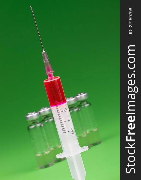 Syringe with red content and medical ampoles on green background. Syringe with red content and medical ampoles on green background