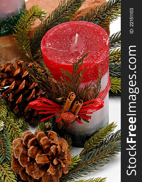 Red, white and green festive candle with green cedar leaves and cinnamon sticks tied on with twine for Christmas. The candle is placed among pine branches and pine cones. Red, white and green festive candle with green cedar leaves and cinnamon sticks tied on with twine for Christmas. The candle is placed among pine branches and pine cones.