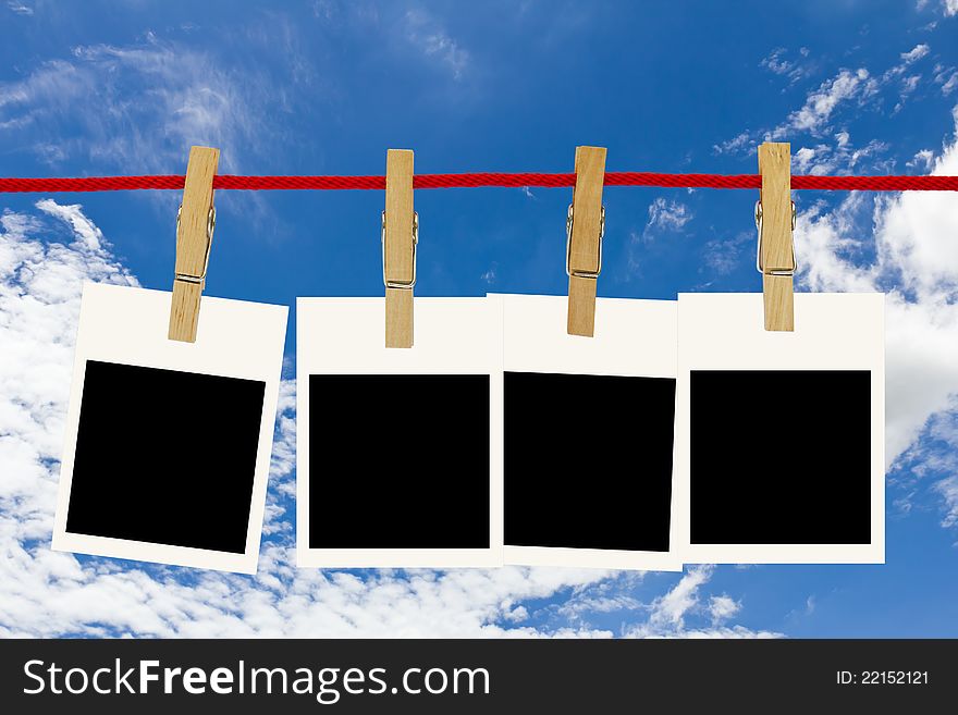 Blank photo frames hang by wooden peg on blue sky