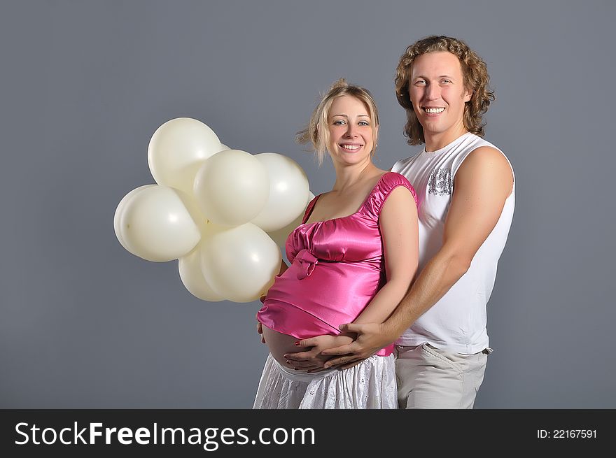 Fashion young couple expecting a baby, gray background with white balloons. Fashion young couple expecting a baby, gray background with white balloons