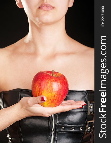 Woman dressed in a leather corset holding a red apple. Woman dressed in a leather corset holding a red apple
