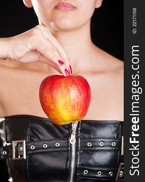 Woman dressed in a leather corset holding a red apple. Woman dressed in a leather corset holding a red apple