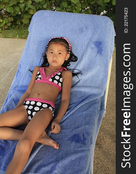 Little chinse girl laying on a chair in a bathing suite. Little chinse girl laying on a chair in a bathing suite