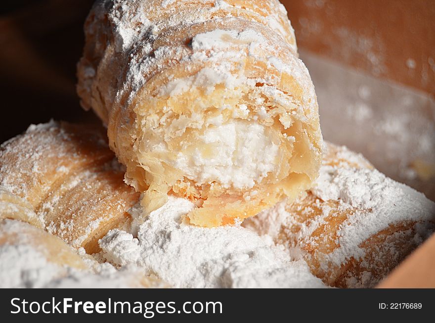 Close-up photograph of cream filled pastries covered in powdered sugar in a brown box. Close-up photograph of cream filled pastries covered in powdered sugar in a brown box.