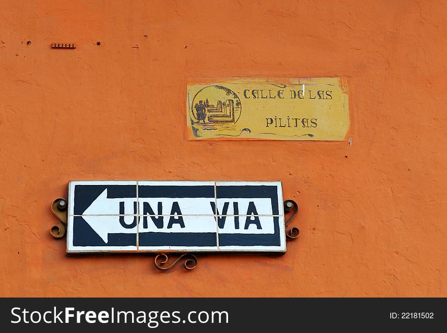 Orange wall with a one way (una via) sign, and a street sign, located in Antigua Guatemala