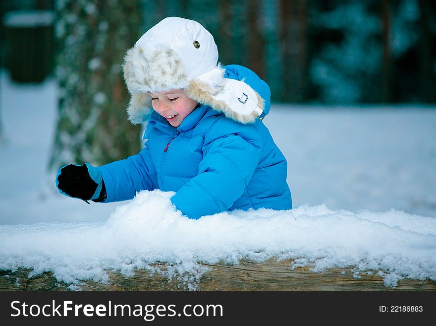 Portrait of a little boy playing with snow outdoors in a winter forest