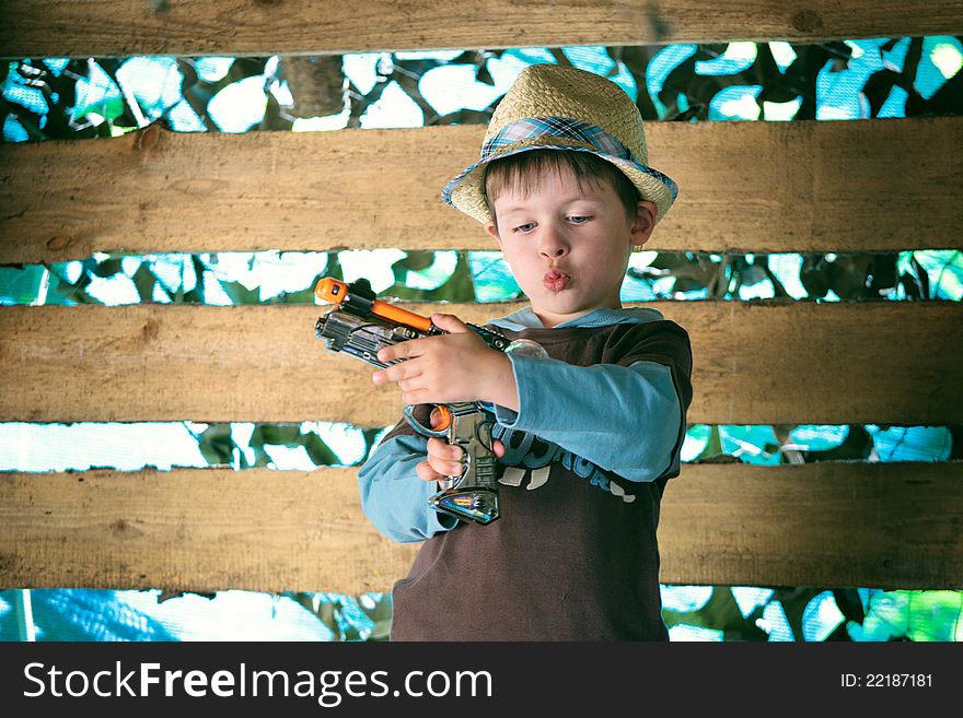 Portrait of a cute boy in hat playing with a pistol