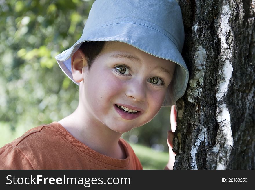 Portrait of an small child boy in a blue sun hat leaning on a birch tree trunk. Portrait of an small child boy in a blue sun hat leaning on a birch tree trunk.