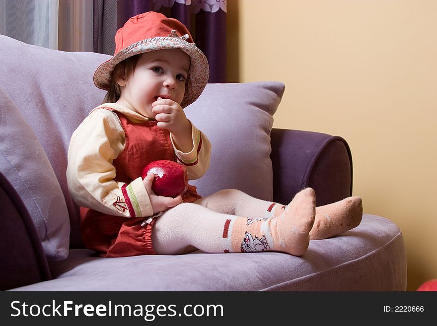 Cute little girl with red apple in her hand sitting on the sofa. Cute little girl with red apple in her hand sitting on the sofa