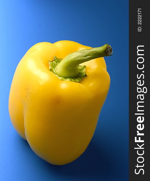 Close-up of brightly yellow pepper with a green pod on a blue background