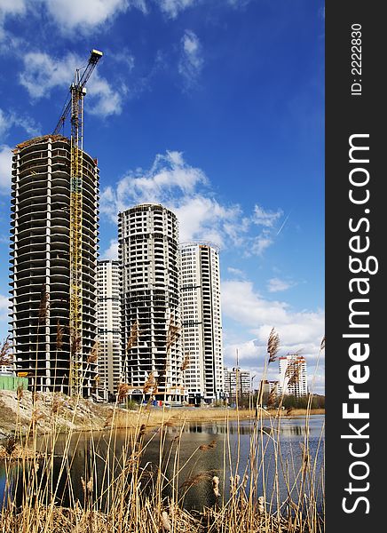 Some under construction skyscrapers in the sky near small lake