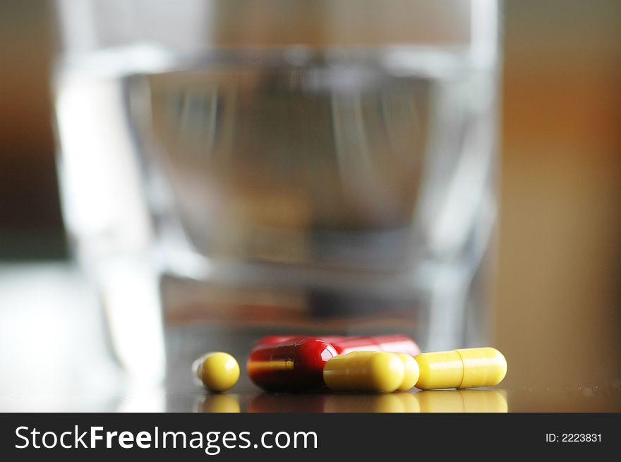 Pills are spread out on table with glass of water in background. Pills are spread out on table with glass of water in background