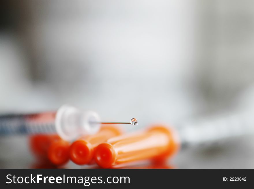 A water drop is at the very end of a syringe. A water drop is at the very end of a syringe
