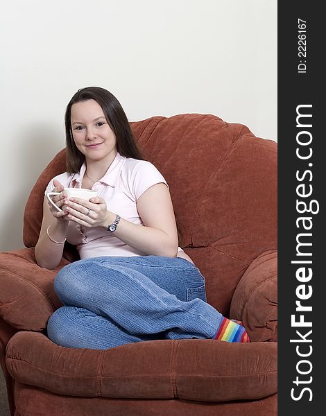 Pretty young woman sitting in a chair holding a cup. Pretty young woman sitting in a chair holding a cup