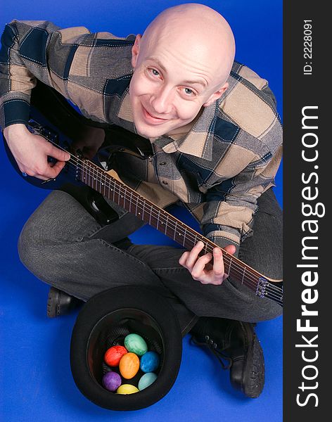 The musician with a guitar and easter eggs sits on a dark blue background. The musician with a guitar and easter eggs sits on a dark blue background