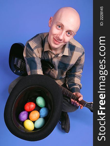 The musician with a guitar and easter eggs sits on a dark blue background. The musician with a guitar and easter eggs sits on a dark blue background
