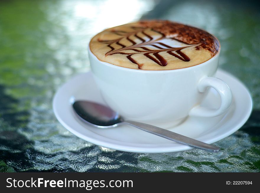 Side view of cappuccino coffee cup with spoon on glass table