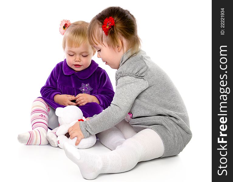 Two girls play with a teddy bear. Isolated on a white background