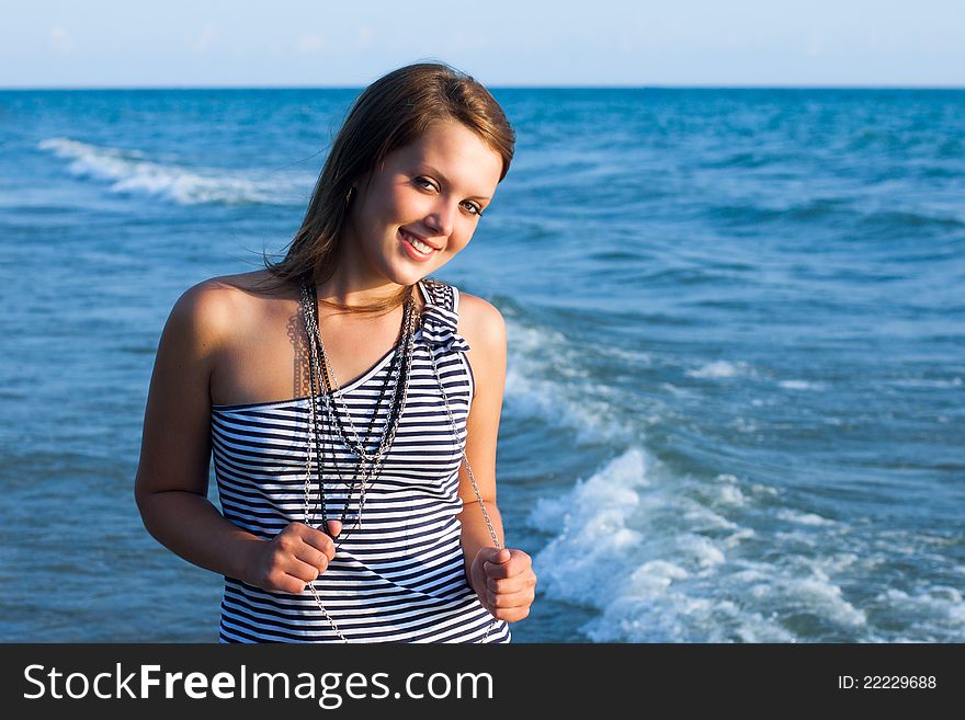 Young pretty girl looking at camers and smiling with the sea as a background. Young pretty girl looking at camers and smiling with the sea as a background
