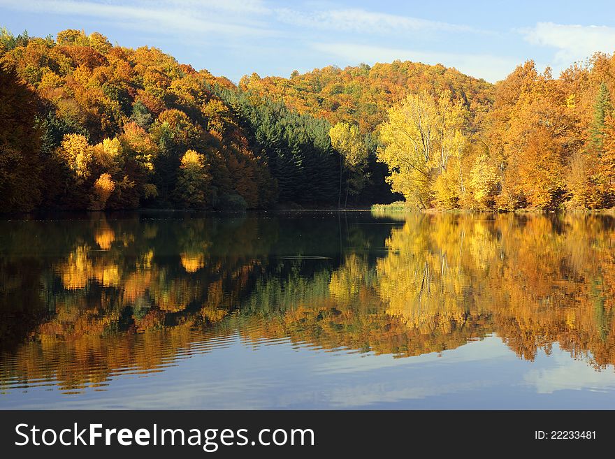 Hills of autumn colors reflected in a calm lake in early morning light