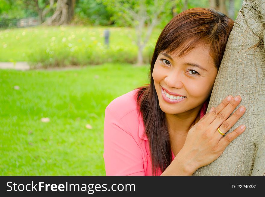 Asian girl smiling and put her hand on tree's trunk in park. Asian girl smiling and put her hand on tree's trunk in park