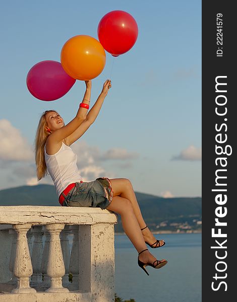 Pretty woman with varicoloured balloons seat on a balcony by the sea