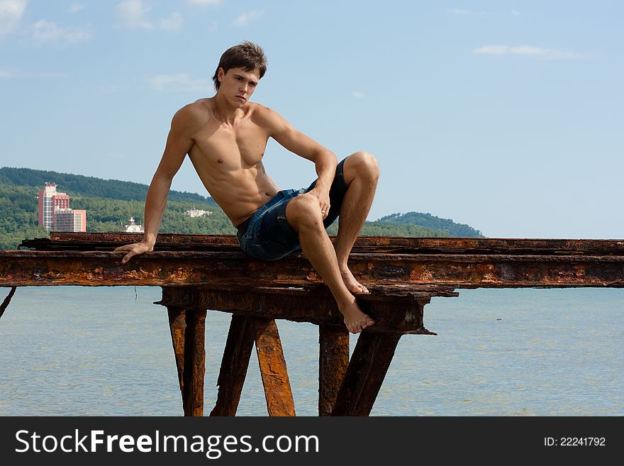 Lad with strong muscles on iron construktion near the sea. Lad with strong muscles on iron construktion near the sea