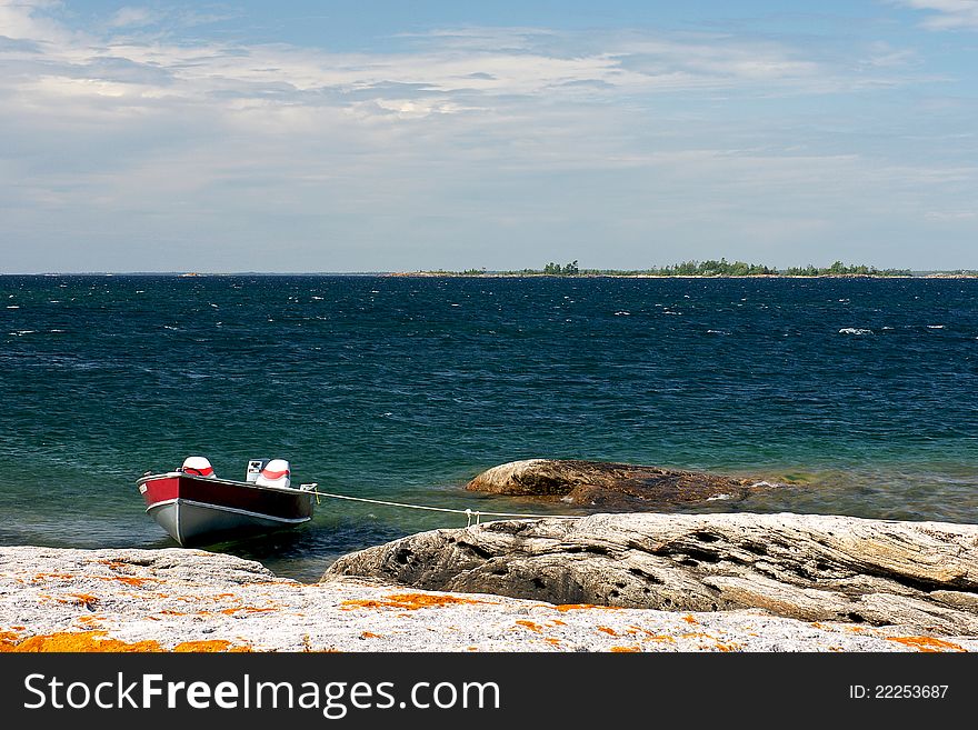 A small aluminum boat moored by a rocky island in Georgian Bay, Ontario. Georgian Bay is known for its azure waters and scenic landscapes and is part of Lake Huron - one of the five Great Lakes.
