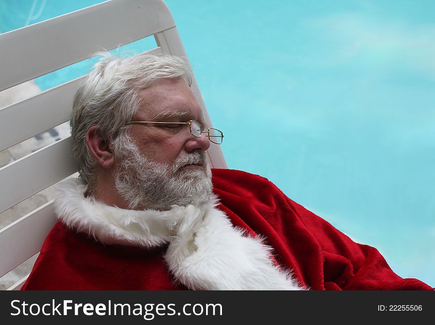 Santa Claus sound asleep on a lounge chair next to a swimming pool. Santa Claus sound asleep on a lounge chair next to a swimming pool.