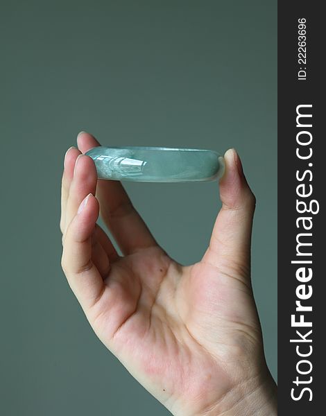 A greenish type A jade / jadeite bracelet holding by female hand towards a grey background. Type A means it has not been treated in any way except surface waxing. A greenish type A jade / jadeite bracelet holding by female hand towards a grey background. Type A means it has not been treated in any way except surface waxing.