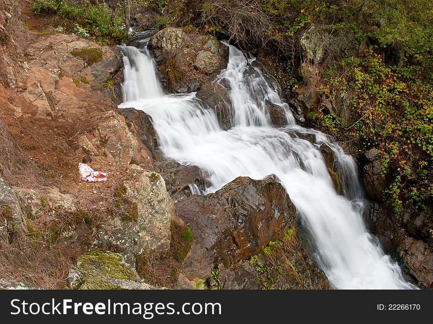 A young baby sits near a water fall cascading down a mountain side. A young baby sits near a water fall cascading down a mountain side.