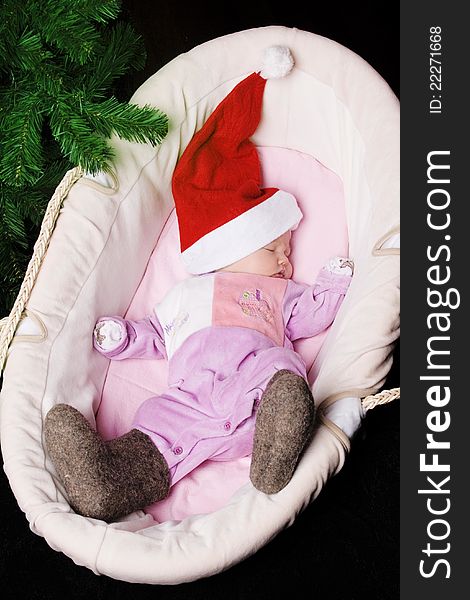 The little baby in winter boots and a hat of Santa Claus sleeps in a basket