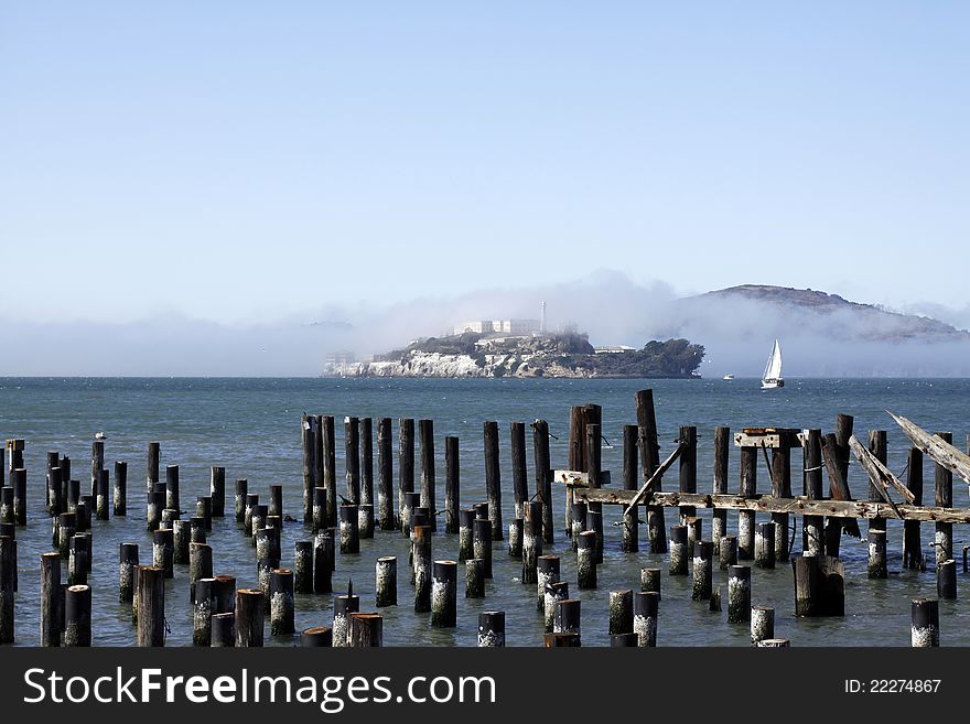 Alcatraz Prison fogged over on a sunny day. Old pilings in foreground. Alcatraz Prison fogged over on a sunny day. Old pilings in foreground.