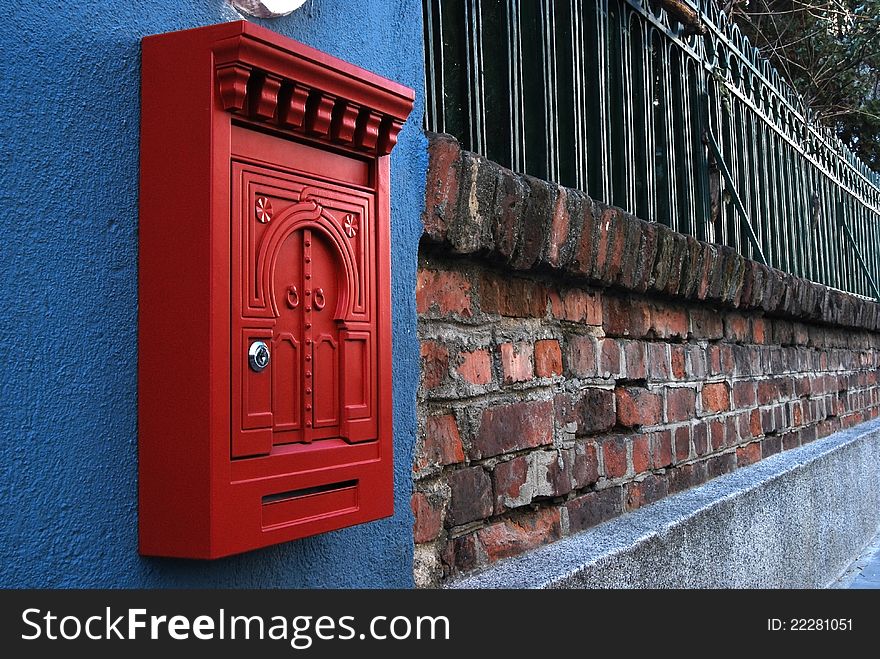 Red metal post box on brick wall and iron fence