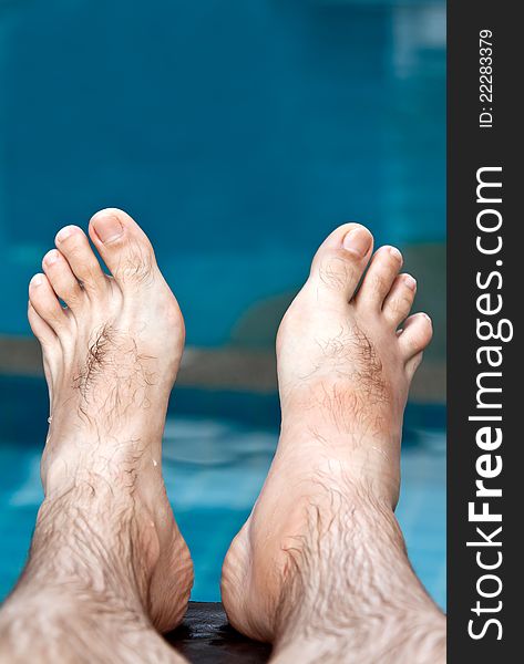 Men's feet on the background of the pool with blue water