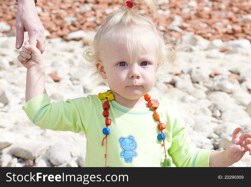 Serious blue-eyed toddler making her first steps while holding on her mother's finger.