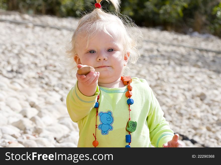 Cute baby girl holding out a pebble to play.