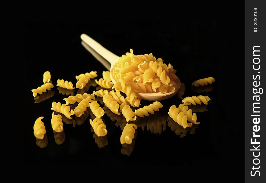 Uncooked pasta and tablespoon on black background