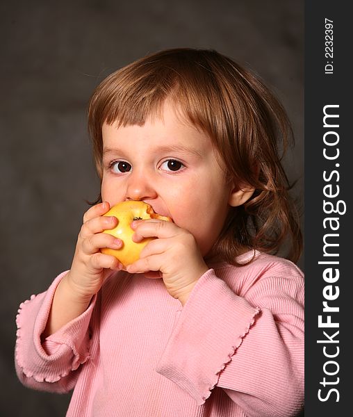 The little girl eats a yellow apple