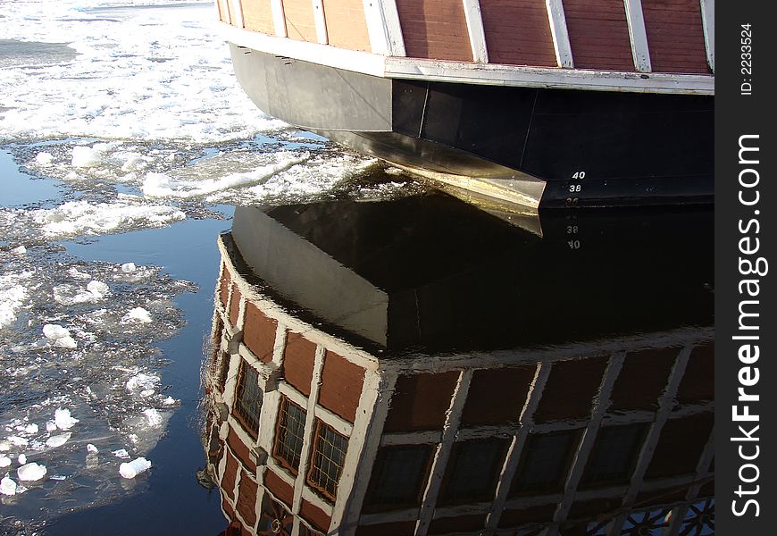 Stern of an ancient ship being reflected in a river's  water covered with ice floes.