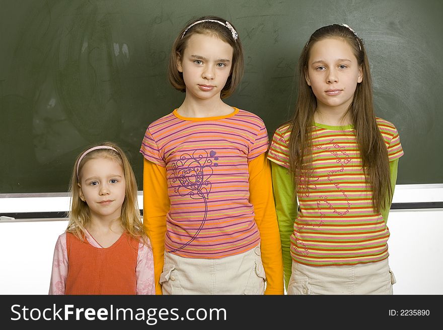 Group of girls (5, 11 and 13yo) are standing and looking at camera. Behind them there's blank greenboard. Group of girls (5, 11 and 13yo) are standing and looking at camera. Behind them there's blank greenboard.