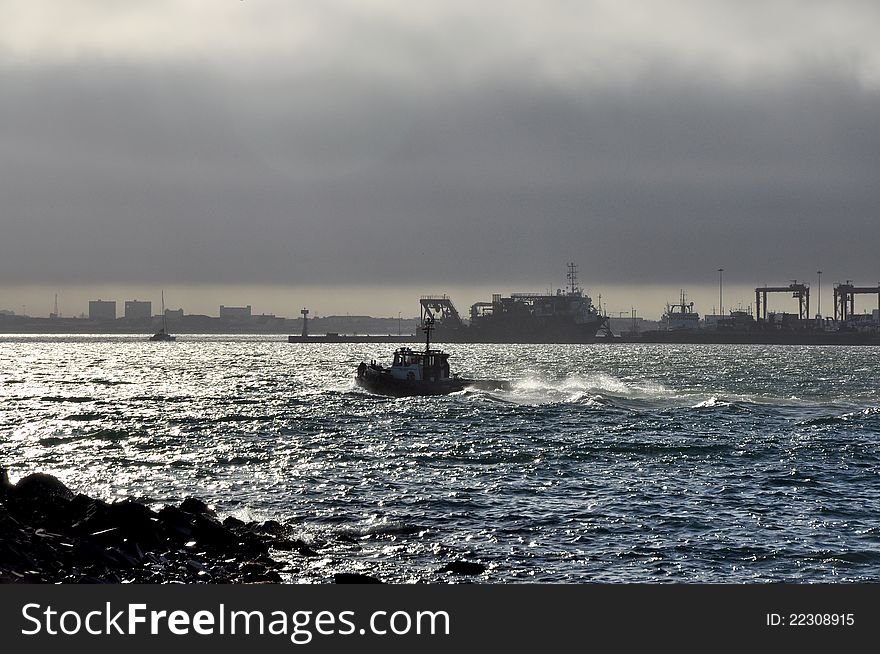 A tug boat leaves Cape Town harbor in choppy waters. A tug boat leaves Cape Town harbor in choppy waters