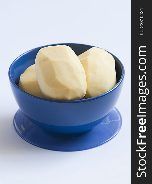 Peeled potatoes 
in blue bowl close up