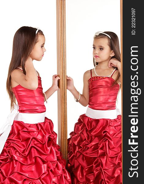 Beautiful little girl in red evening dress in front of mirrow on white background