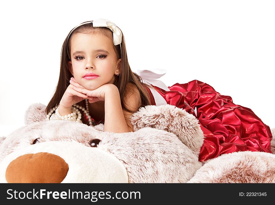 Beautiful little girl in red evening dress lying on big toy on white background