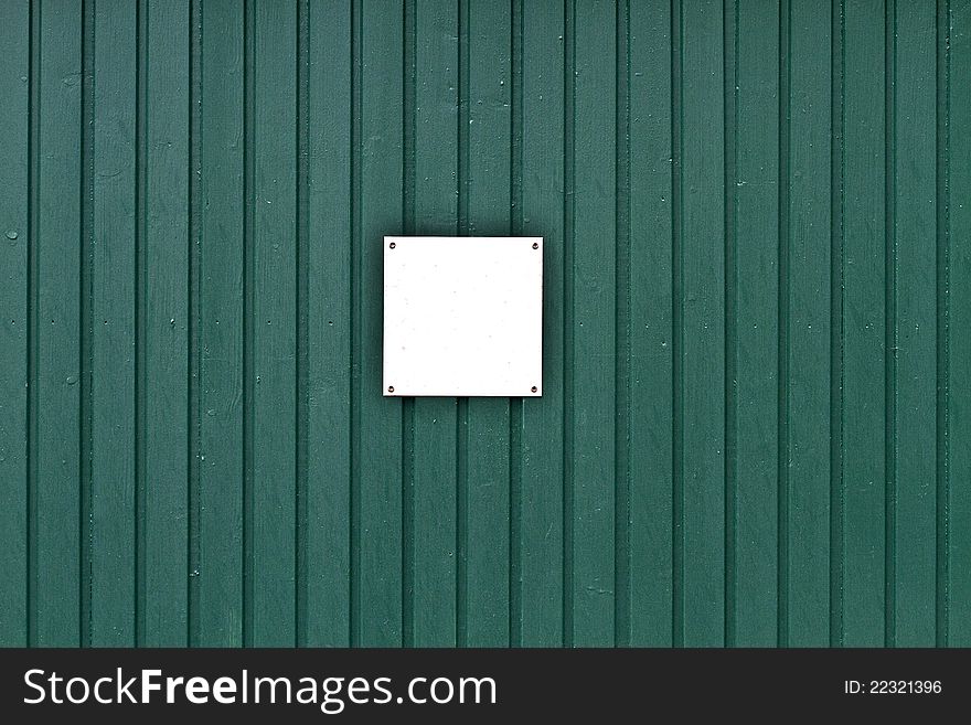 Small blank sign on green wooden wall.