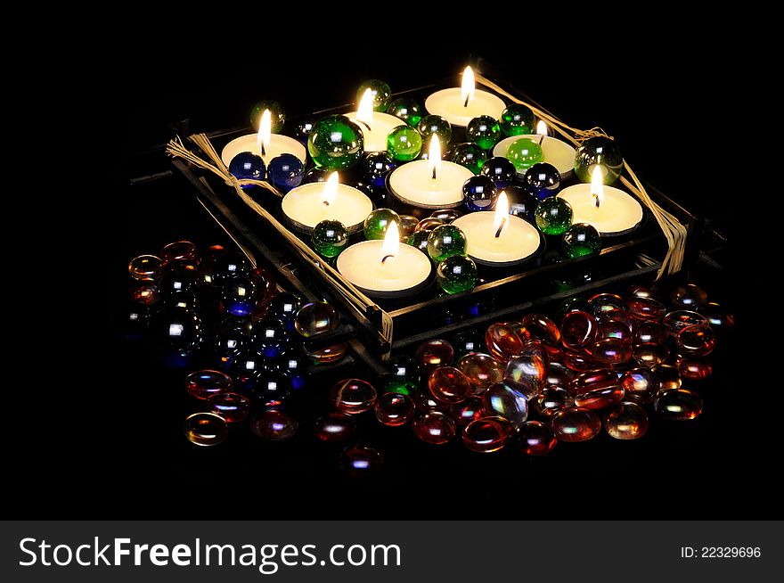 Burning romantic candles in a candle holder with decorative multicolored glass stones on a black background. Burning romantic candles in a candle holder with decorative multicolored glass stones on a black background