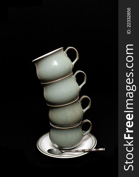 Four green tea cups balancing on a white saucer with a black background. Four green tea cups balancing on a white saucer with a black background