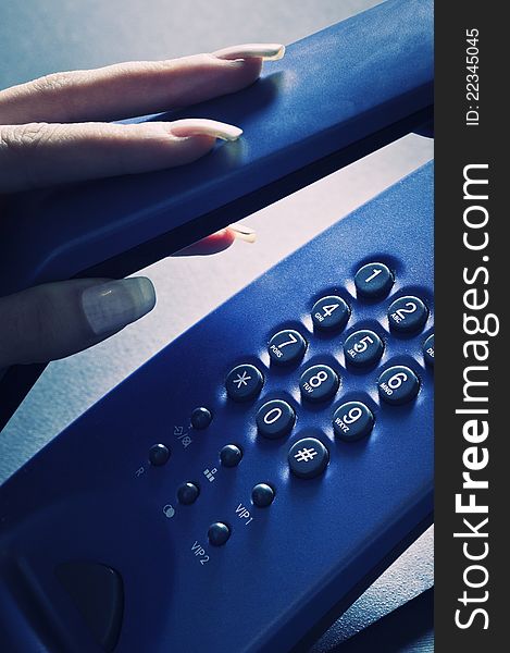 A woman's hand picking up the handset of an  blue phone. A woman's hand picking up the handset of an  blue phone